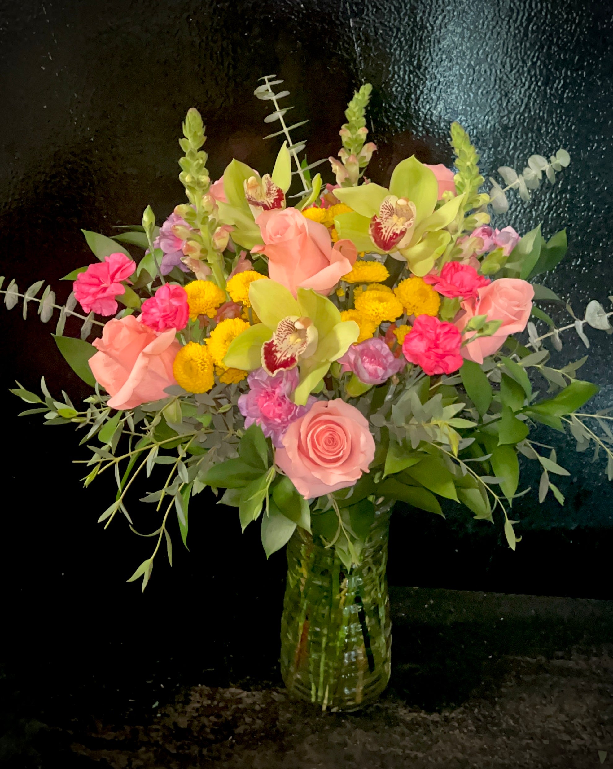 Mixed, moderate sized arrangement of flowers in a taller clear vase.