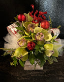 Decorative floral arrangement with green orchids, red ornaments, and festive ribbon  arranged in a small wood box.