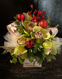 Decorative floral arrangement with green orchids, red ornaments, and festive ribbon  arranged in a small wood box.
