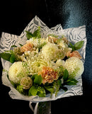 A wrapped, mixed floral bouquet in a neutral palette.