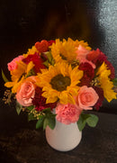 Sunflowers and roses with mixed blooms in a ceramic vase.